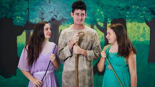 Tres estudiantes de la Shalom Christian Academy están juntos en el área exterior verde con árboles de fondo.