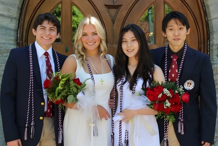 Cuatro estudiantes de la Shattuck-St. Mary's School están de pie frente a un arco de piedra y sostienen rosas rojas en la mano.