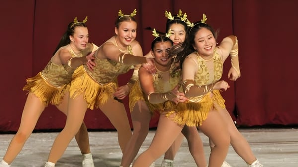 Cinco estudiantes de la Shattuck-St. Mary's School actúan en trajes dorados frente a un telón rojo en un escenario.
