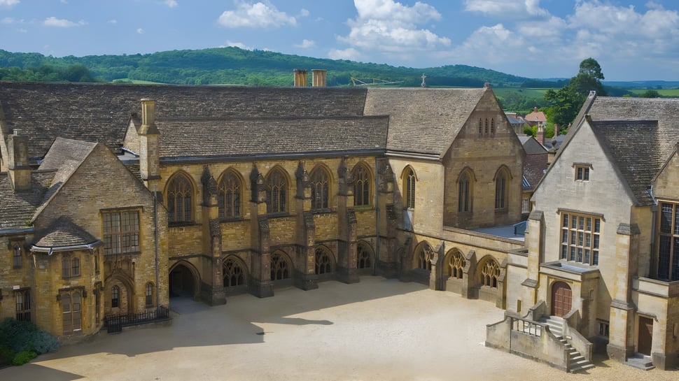 Una ciudad medieval con una gran estructura parecida a una catedral frente a colinas boscosas en el terreno de la Sherborne School.