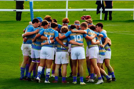 Un grupo de jóvenes atletas en camisetas azules y blancas se reúne en el campo de deportes de la Sherborne School.