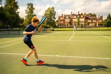 Una estudiante juega al tenis en el cuidado campo de tenis de la Sherfield School frente a un edificio histórico.