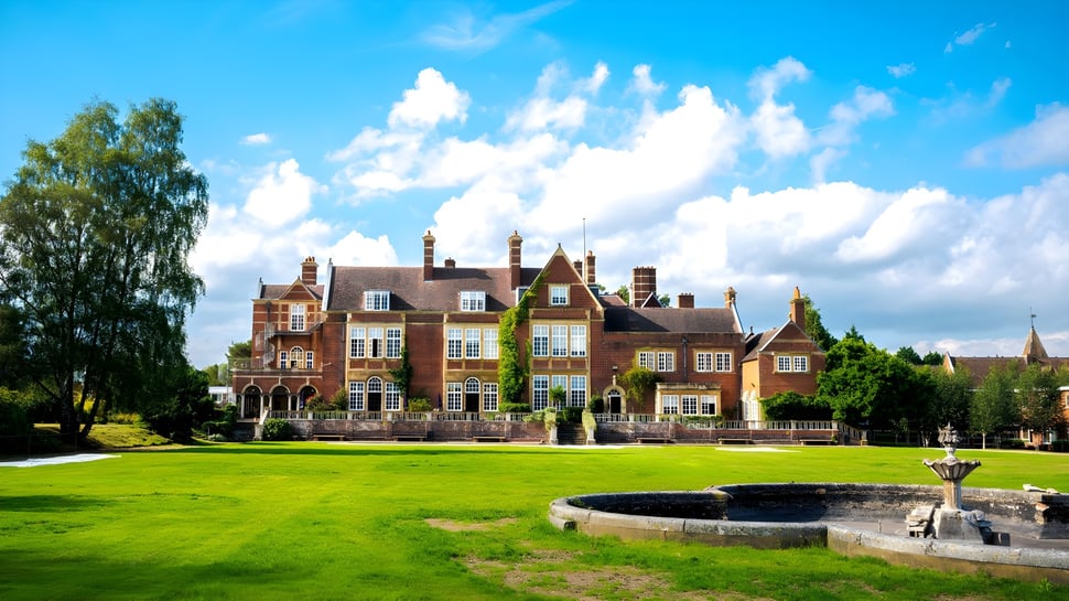 El impresionante edificio de ladrillo de la Sherfield School con torres se encuentra frente a un césped verde y una fuente en primer plano.