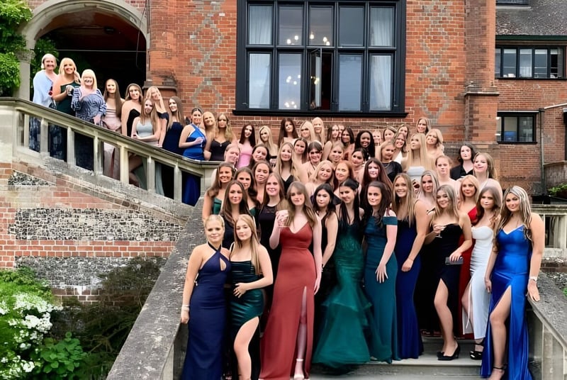 Un grupo de jóvenes mujeres vestidas formalmente se encuentra frente a un edificio histórico de ladrillo en el campus del Shiplake College.