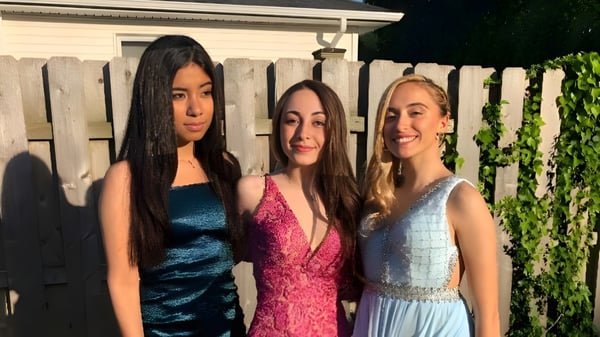 Tres alumnas de la Shore Regional High School posan frente a una valla de madera con vegetación verde de fondo.