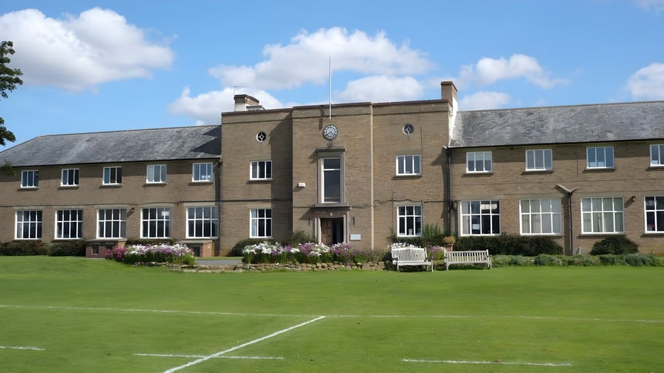 El edificio de ladrillo de la Sibford School con reloj se encuentra detrás de un césped y jardín bien cuidados.
