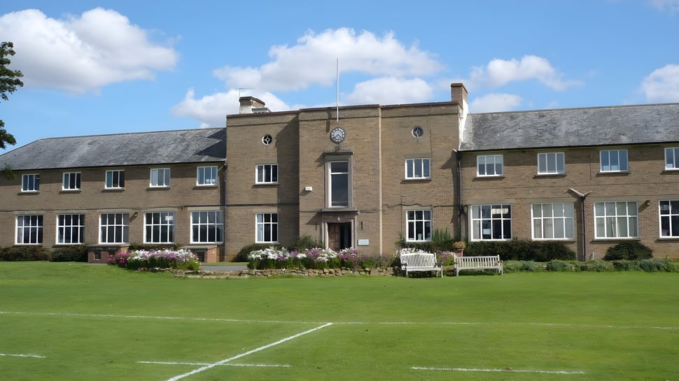 El gran edificio de ladrillo con reloj de la Sibford School se encuentra detrás de un césped y jardín bien cuidados.