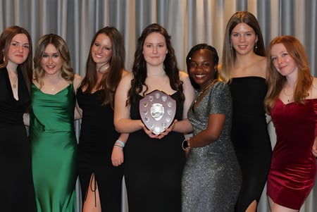 Un grupo de mujeres con ropa formal posan frente a una cortina gris en el campus de la Sibford School.