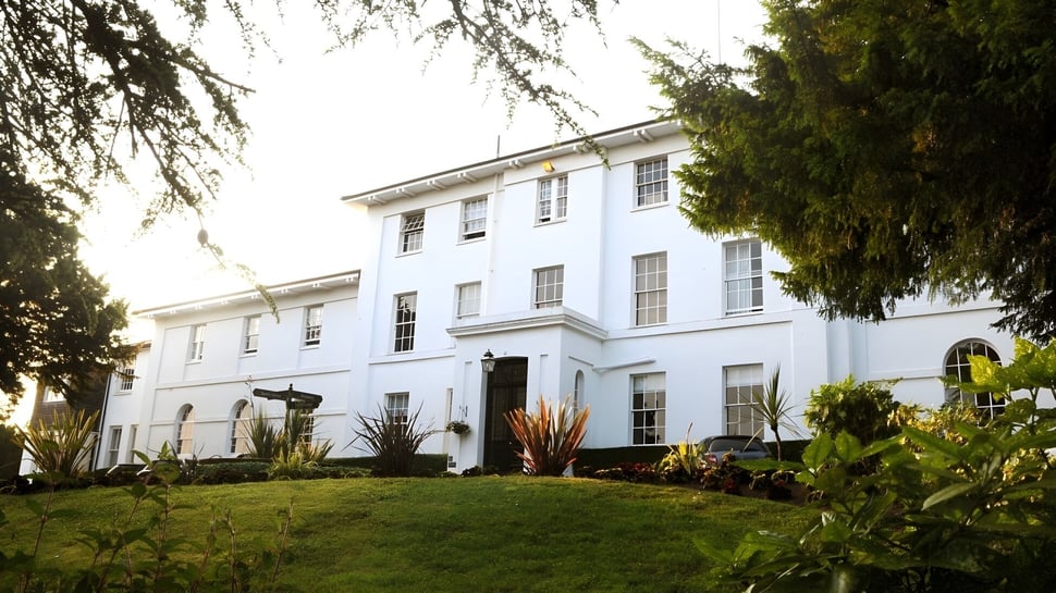 La blanca casa principal de la Sidcot School se encuentra frente a un césped bien cuidado y rodeada de altos árboles.