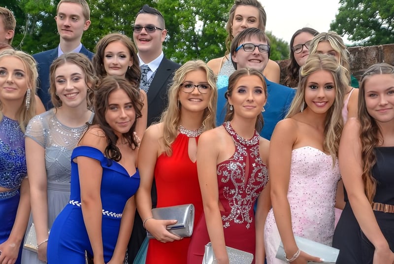 Un grupo de jóvenes en ropa formal posan afuera frente a árboles en el terreno de la Sidcot School.