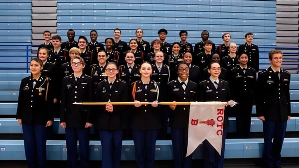 Un grupo de estudiantes del Sierra Vista Unified School District está con uniformes negros frente a un fondo azul-gris y sostiene un banner.
