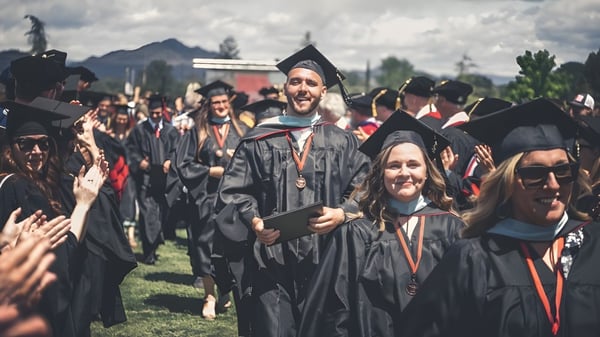 Un grupo de graduados de la Simpson University lleva togas y birretes negros en una ceremonia de graduación al aire libre.