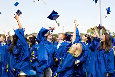 Un grupo de graduados de Sioux Falls Christian School lanza sus birretes azules al aire bajo un cielo despejado.