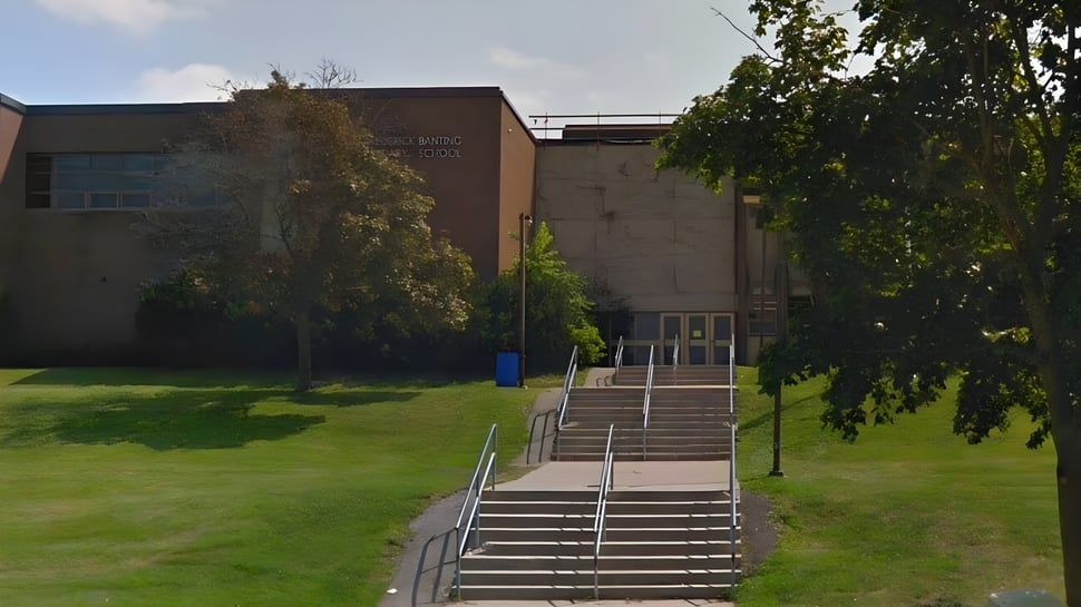 El edificio de ladrillo con escaleras en la entrada del terreno de la Sir Frederick Banting Secondary School está rodeado de una superficie de césped y árboles.
