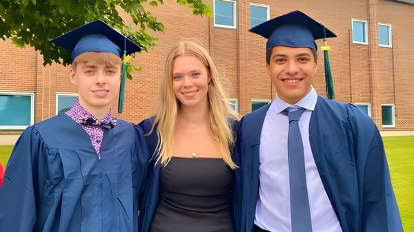 Tres estudiantes de la Sir Wilfred Laurier Secondary School celebran su graduación frente a un edificio de ladrillo.