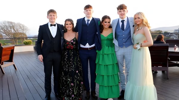Un grupo de personas con ropa formal está de pie en la terraza de madera en el terreno de la Sligo Grammar School frente a un paisaje escénico.