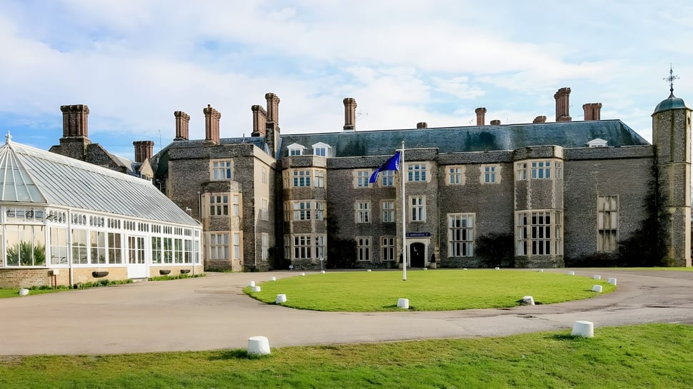La histórica casa señorial con invernadero y césped cuidado en el campus del Slindon College bajo un cielo nublado.