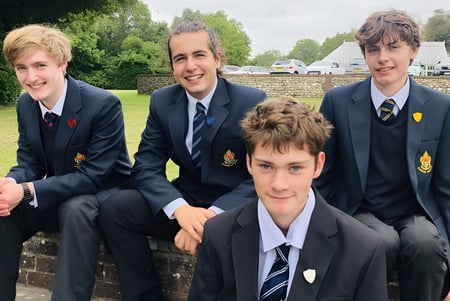Cuatro estudiantes masculinos en uniforme escolar están sentados en un banco al aire libre en el campus del Slindon College.