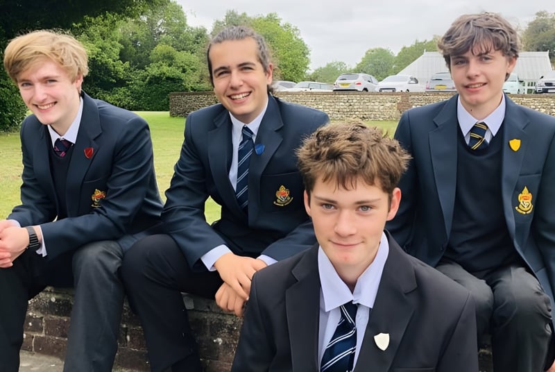 Cuatro estudiantes en uniforme escolar están sentados juntos en un banco al aire libre en el campus del Slindon College.