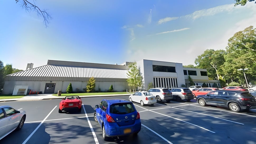 El moderno edificio escolar de la Smithtown Christian School con estacionamiento y árboles en primer plano bajo un cielo azul.