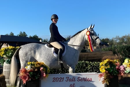 Una estudiante de la Solebury School monta un caballo blanco en el exterior con flores y un cartel de la Serie de Otoño 2021.