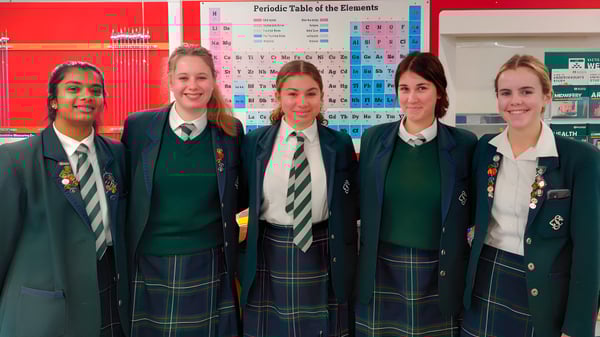 Cinco alumnas en uniforme escolar están frente a un sistema periódico en la pared del Solway College.