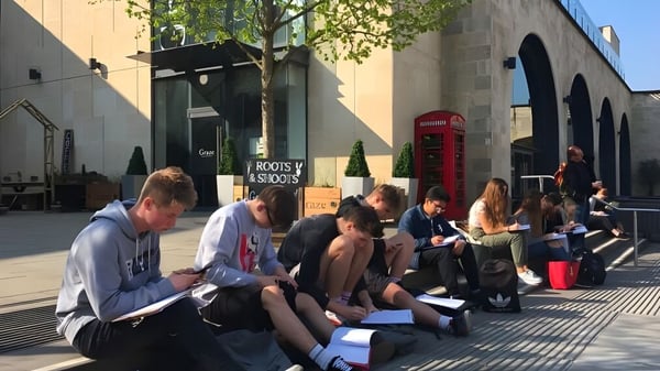 Un grupo de jóvenes está sentado en la acera frente a un edificio en el campus de la Somerset Studio School.