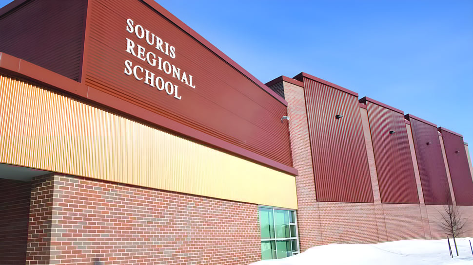 El gran edificio de ladrillo rojo de la Souris Regional School se ve bajo un cielo despejado con nieve en primer plano.