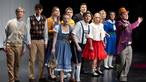 Un grupo de estudiantes está en trajes coloridos en un escenario de la South Christian High School.