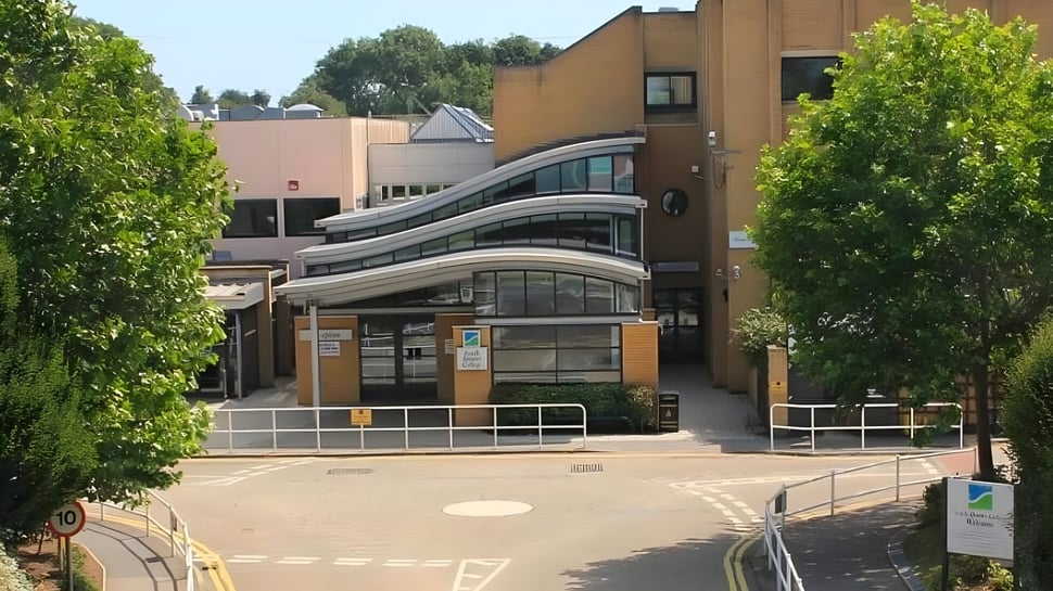 El moderno edificio del South Downs College está rodeado de árboles verdes y se puede acceder a él por un camino pavimentado.