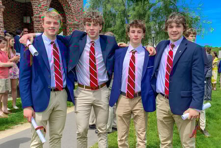 Un grupo de estudiantes con trajes azules y corbatas rojas está frente a un edificio de ladrillo en el campus de la South Kent School.