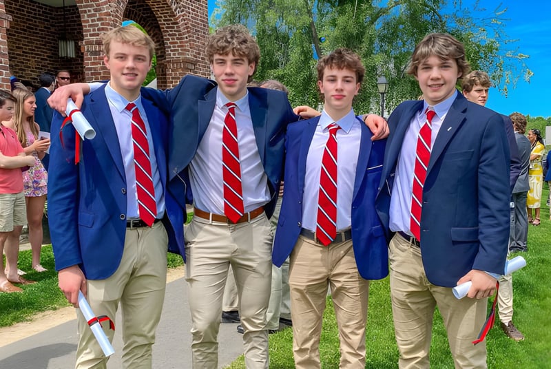 Un grupo de estudiantes con trajes azules y corbatas rojas está frente a un edificio de ladrillo en el campus de la South Kent School.