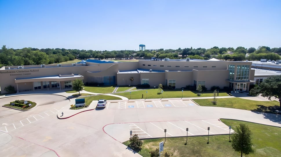 El moderno edificio principal de la Southwest Christian Academy con torre de agua y área verde circundante con caminos.