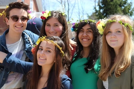 Un grupo de estudiantes de la Sparhawk School sonríe con coronas de flores frente a un edificio en el campo.