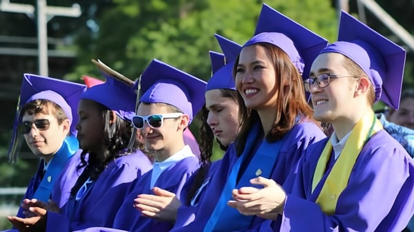 Un grupo de graduados en togas moradas celebra su graduación en el terreno de la Sparhawk School.