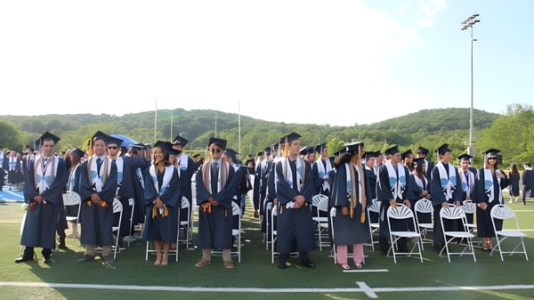Graduados de Sparta High School en vestimenta académica están de pie en un campo con un bosque y un cielo despejado de fondo.