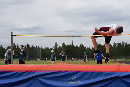 Un estudiante de la Sparwood Secondary School salta con un traje rojo sobre una barra alta en el salto de altura al aire libre.