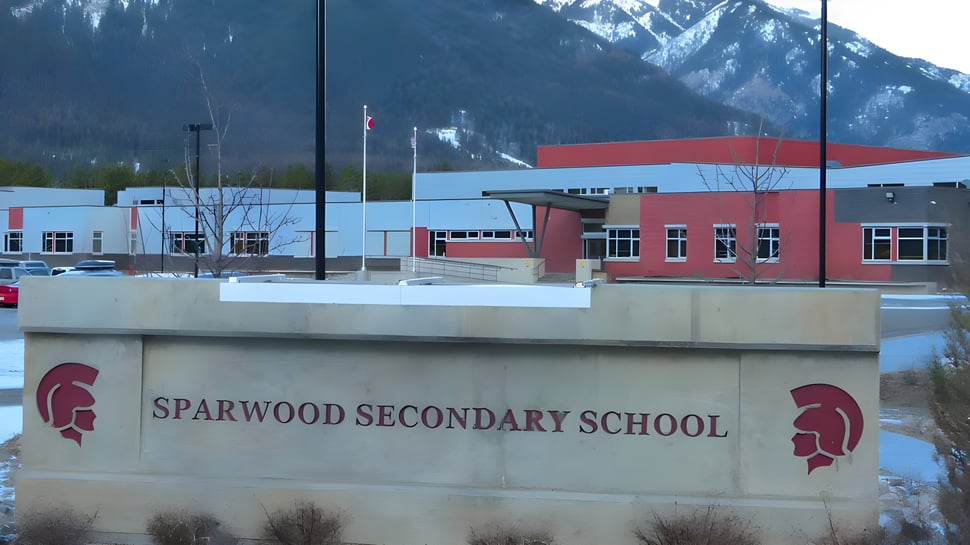 El moderno edificio escolar de la Sparwood Secondary School con fachada roja y blanca frente a montañas cubiertas de nieve.