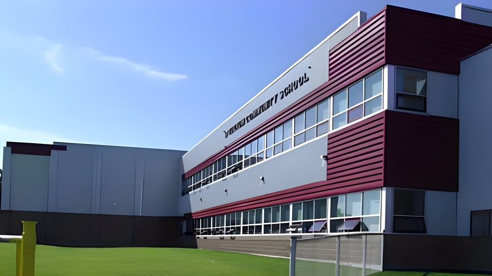 El moderno edificio de varios pisos de la Spectrum Community Secondary School con fachada roja y blanca está rodeado de un prado verde.