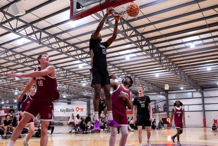 Dos estudiantes de la SPIRE Academy luchan en la cancha de baloncesto por el balón frente a los espectadores.