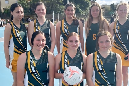 Un grupo de jóvenes atletas del Spotswood College posan juntas en el campo deportivo con un balón de baloncesto en primer plano.