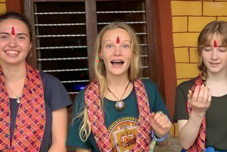 Tres alumnas de la Spring Street International School muestran expresiones faciales enérgicas frente a una pared de ladrillos amarillos.