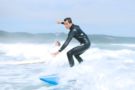 Una persona con un traje de neopreno negro surfa en una ola en el océano con montañas al fondo en el terreno de la Springbank School.
