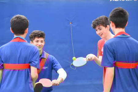 Estudiantes del Springbank Secondary College juegan un partido de tenis de mesa frente a un fondo azul.