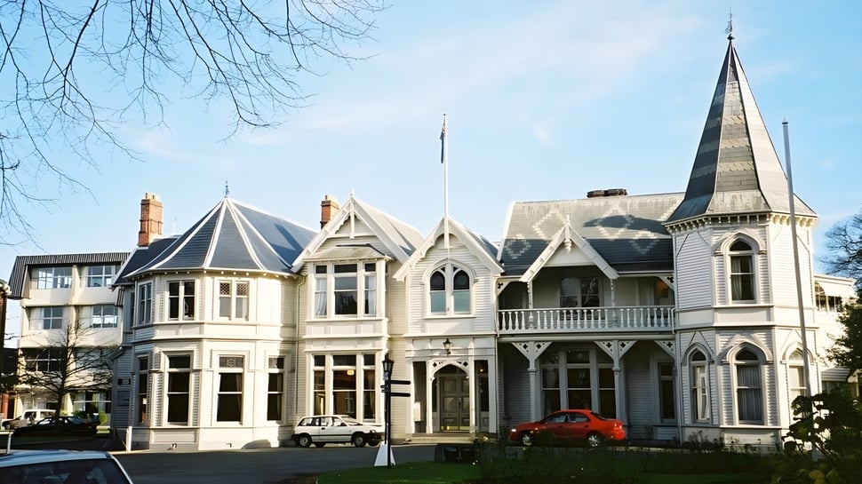 El edificio principal victoriano del St. Andrew's College con fachada ornamental frente a un cielo azul y árboles sin hojas.