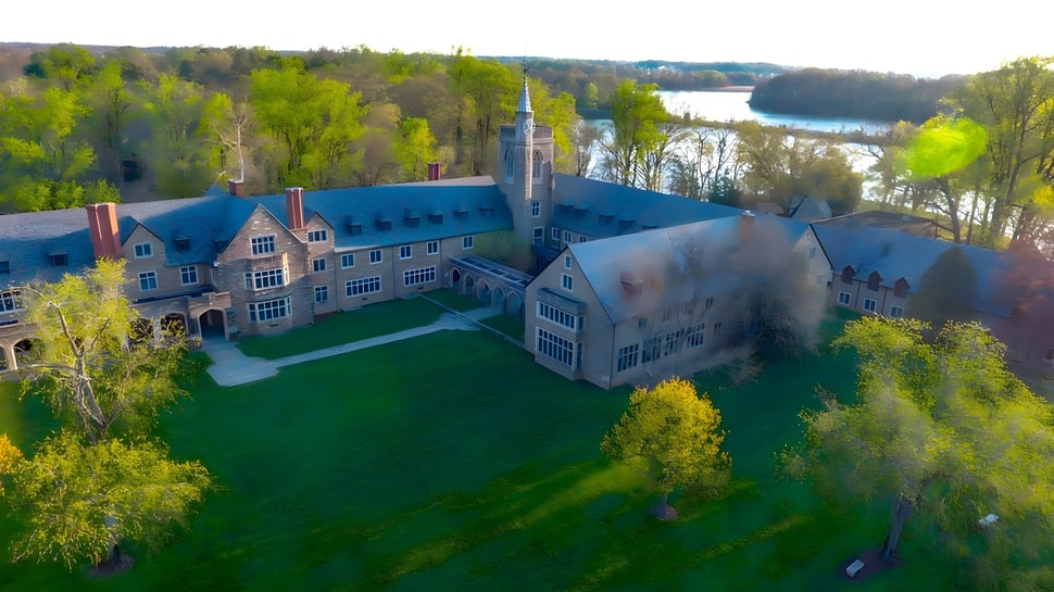 La histórica arquitectura castillo de la St. Andrew's School se encuentra en un prado verde con un bosque y un lago al fondo.