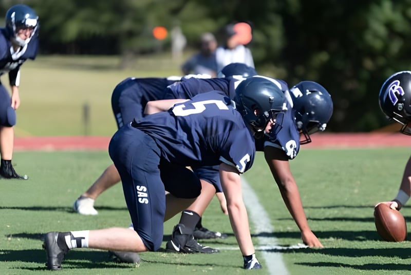 Un grupo de jugadores de fútbol americano de la St. Andrew's-Sewanee School está en posición defensiva en un campo de hierba.