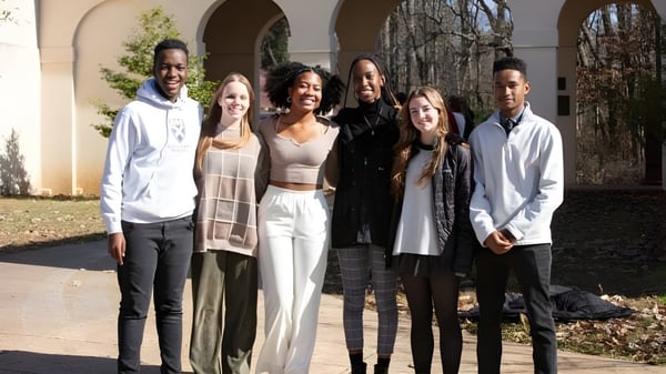 Un grupo de estudiantes está frente a un edificio con ventanas de arco en el terreno de la St. Andrew's-Sewanee School.