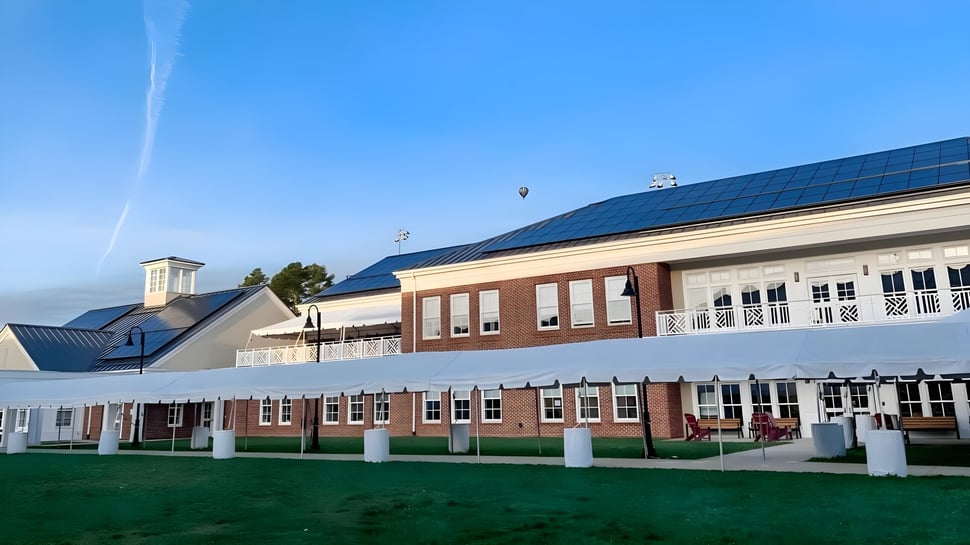 El edificio de ladrillo de varios pisos de la St. Anne's-Belfield School con paneles solares en el techo y césped circundante bajo un cielo azul.