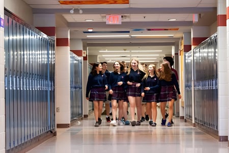 Un grupo de jóvenes alumnas en uniformes escolares camina juntas por el pasillo bien iluminado de la St. Anne's Catholic School.